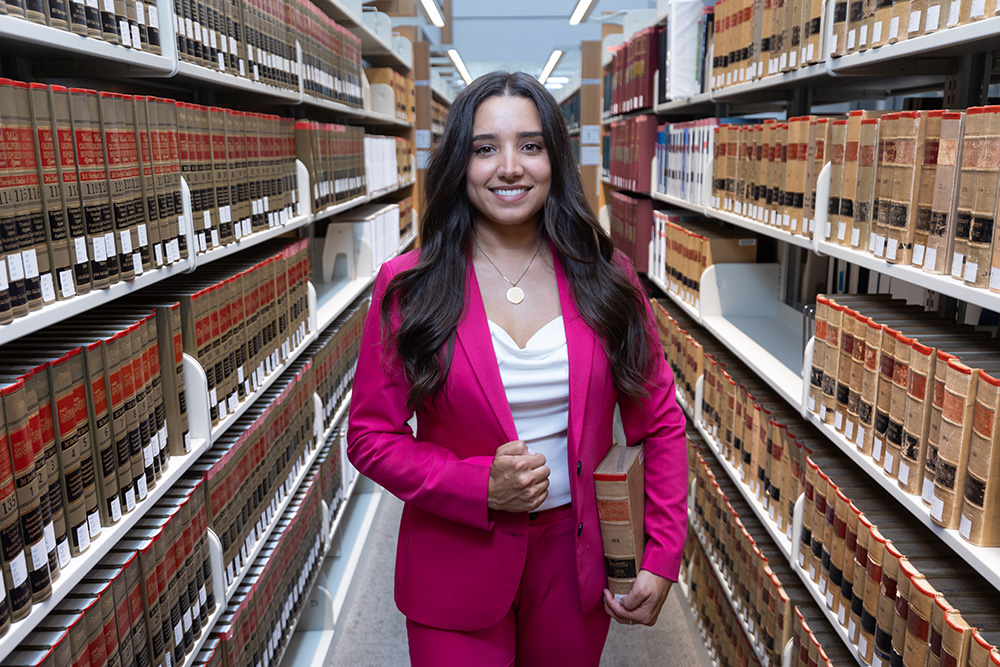 Mirelle Raza poses for a portrait at Charney Hall at Santa Clara University, standing between two shelves of books in the law library.