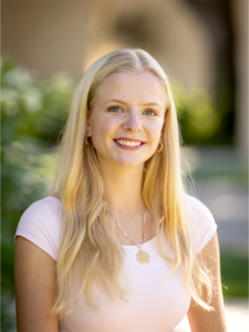 Katie Duffy in light pink shirt, blurred background in Mission Garden on Santa Clara campus.