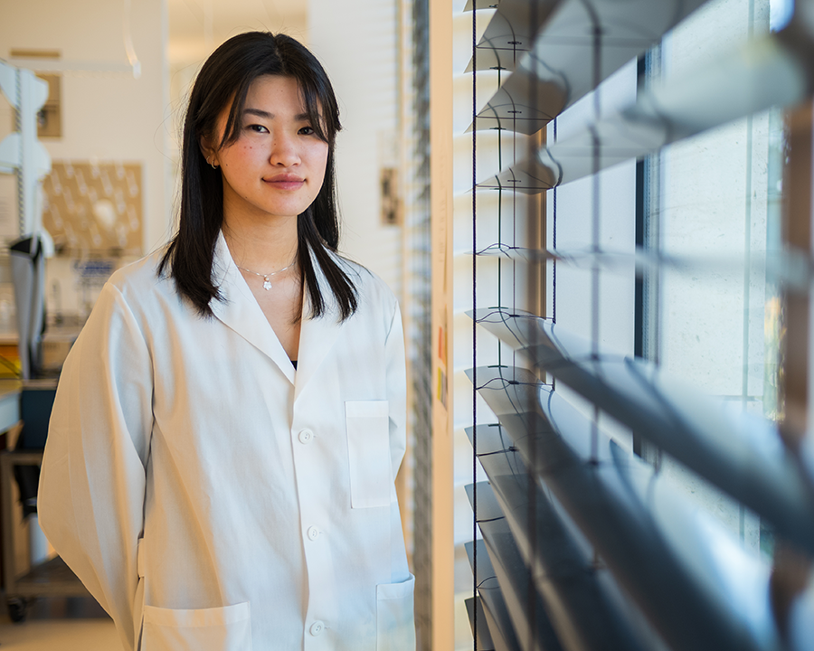 Samantha Lei, a young asian woman wearing a white lab coat looks to the camera.