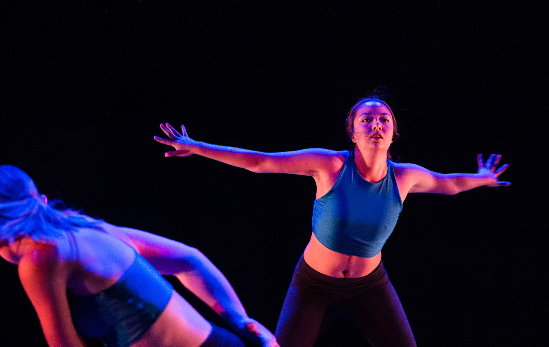 Young woman dances on stage with her arms outstretched horizontally.