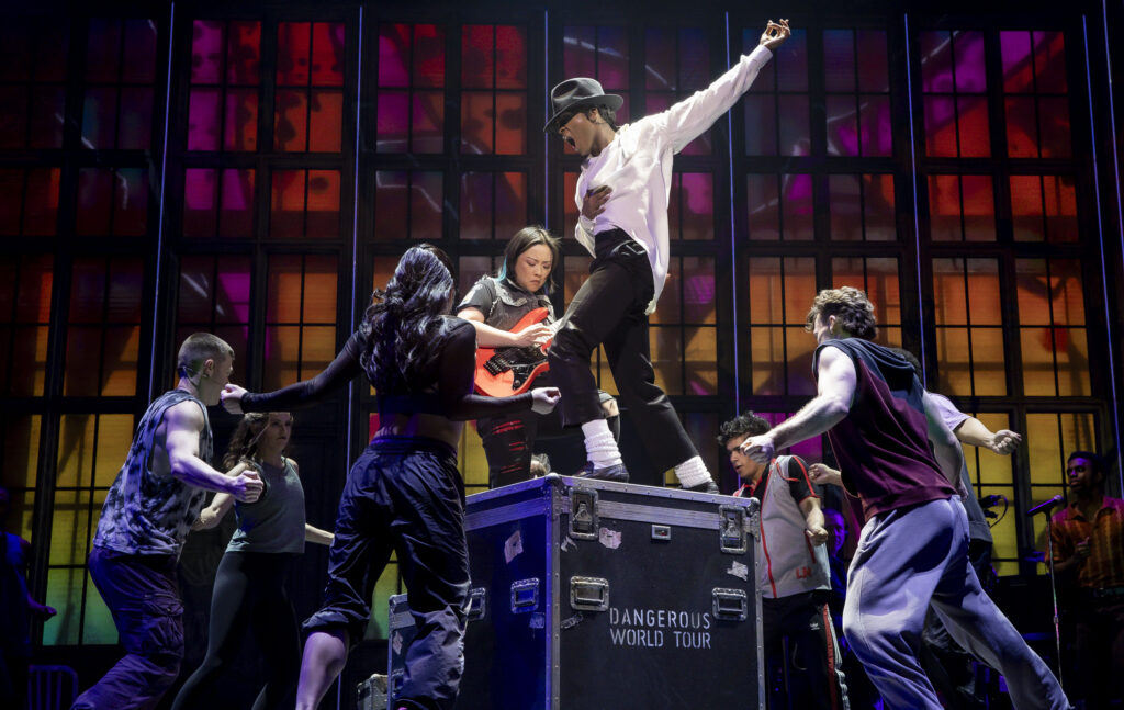 A photo of a performance of MJ at The Tonys. The actor playing Michael Jackson is standing on top of a black box as six other performers stand around the box.