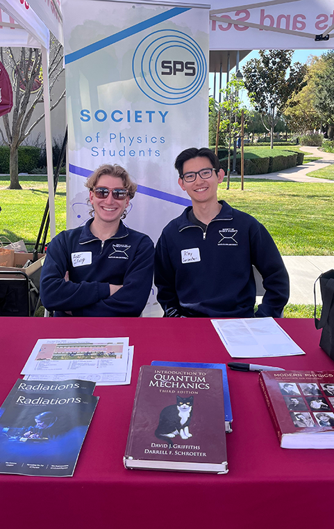 Two male students sit at a tabling event advertising the Society for Physics Students.