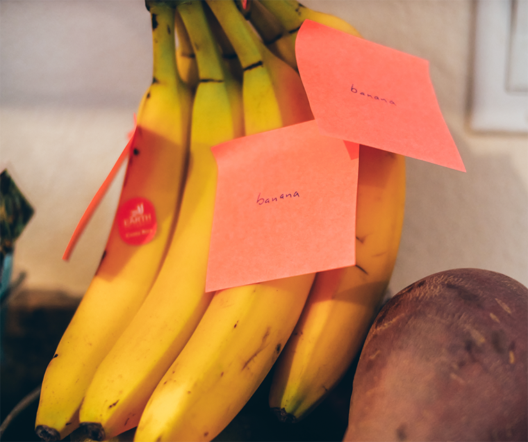 A bunch of bananas sit on a kitchen counter, with three stickie notes says banana on them.
