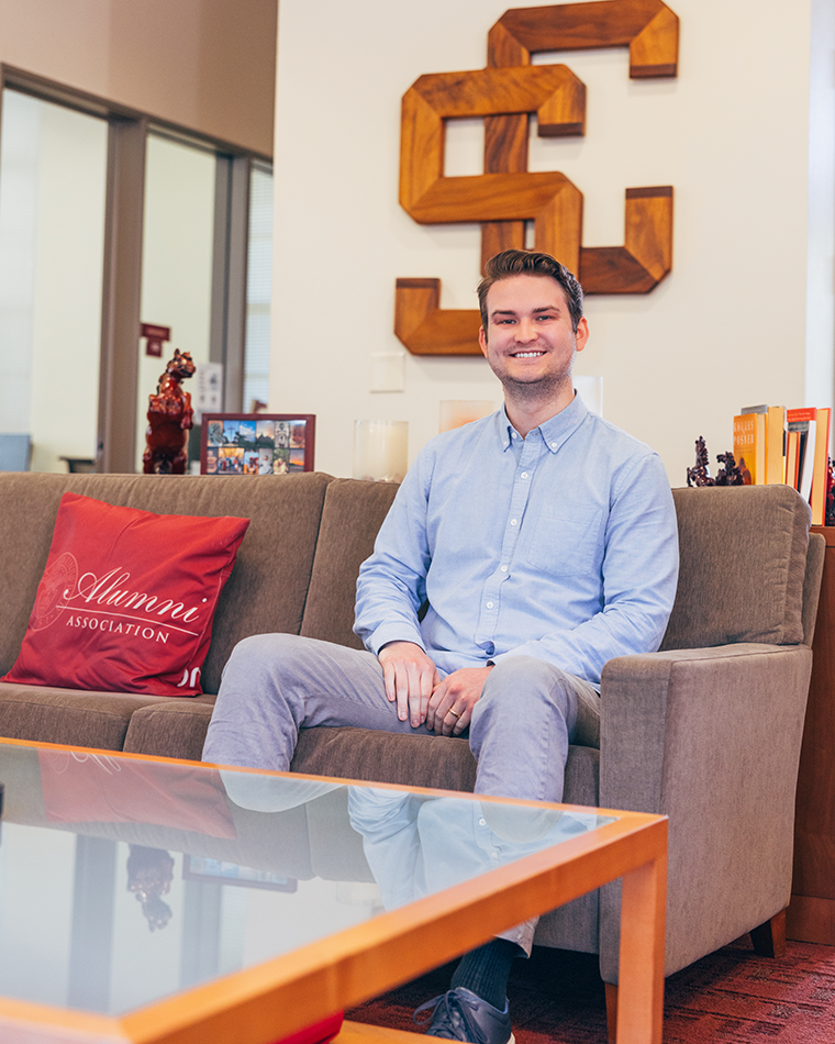 A man in a blue button-up sits casually on a couch.