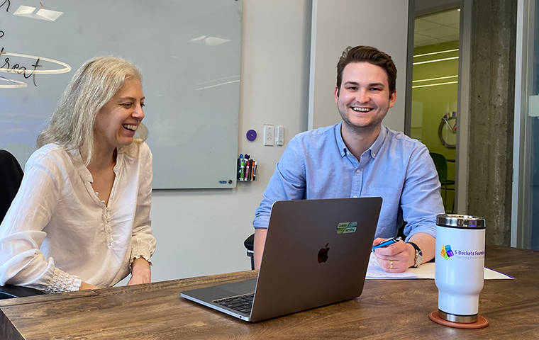 A woman and a man smile while working together at a laptop.