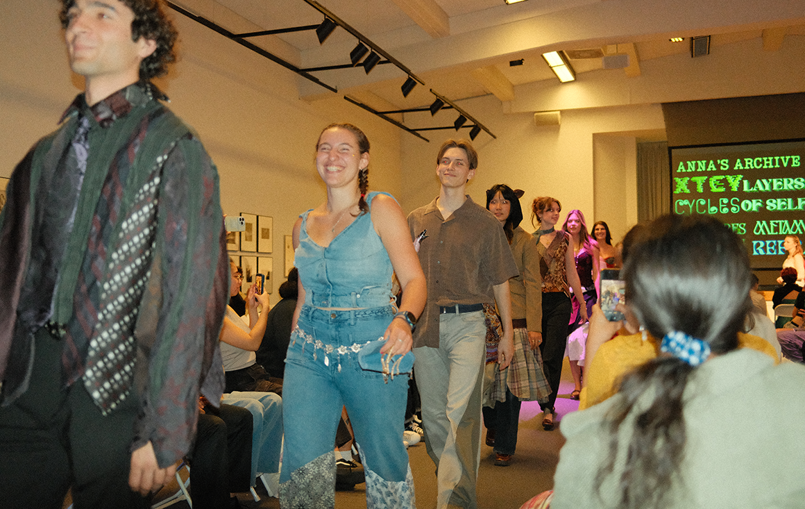 A line of models wearing ties, denim, and other unique materials walking down an runway.