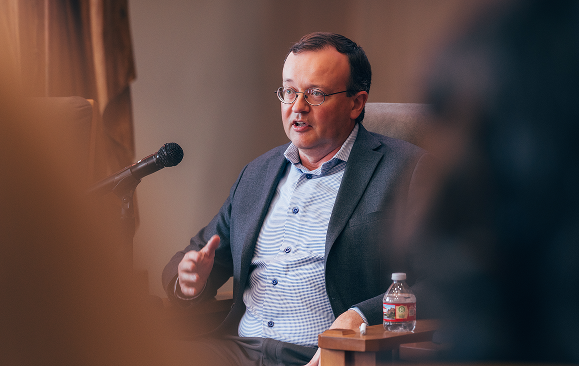 A man in glasses speaks into a microphone.