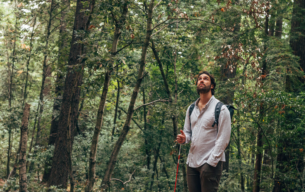 A young man with long hair and a beard wearing a button up shirt, walking through the words.