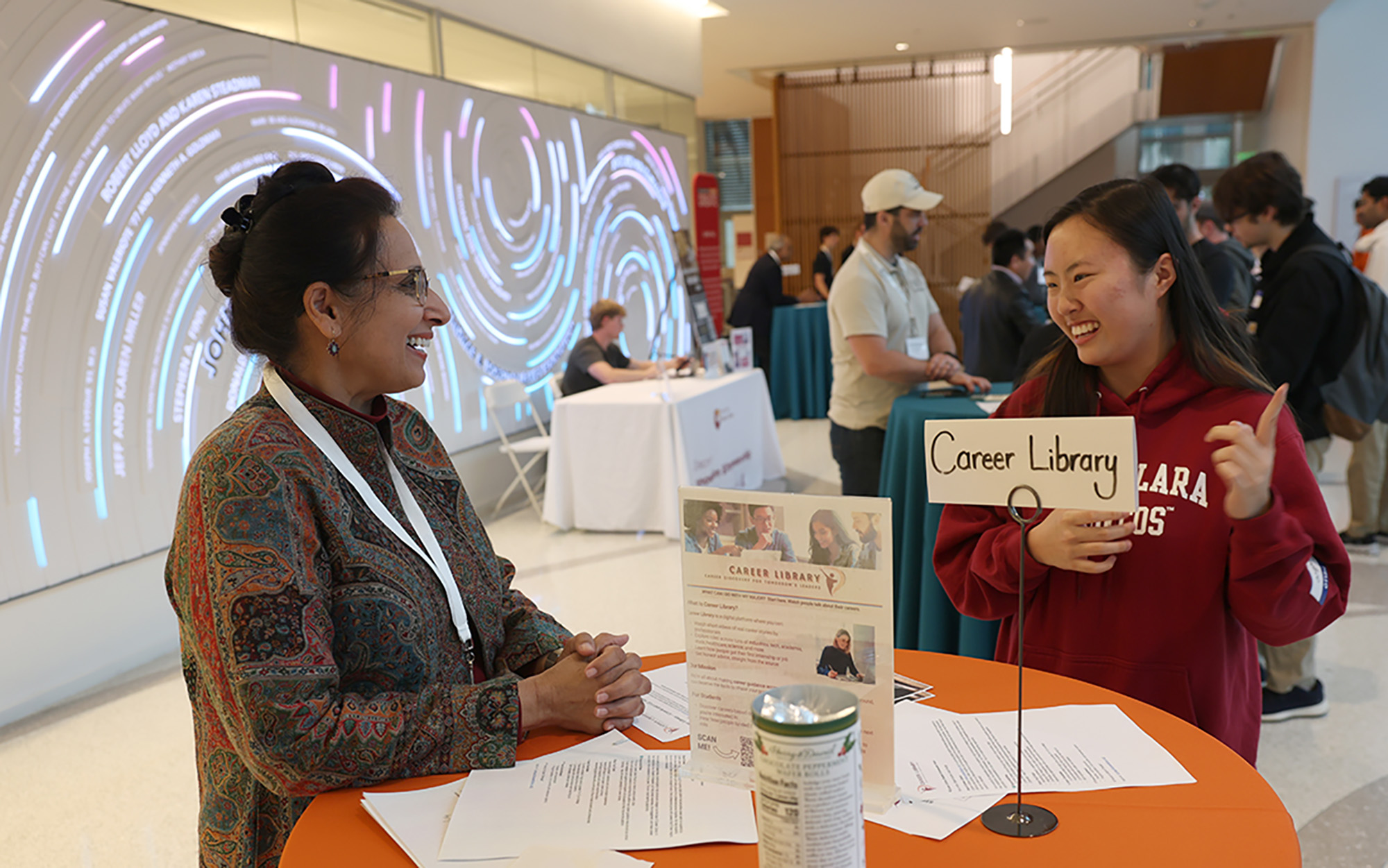 A student speaks with a participant in a Santa Clara Career Fair in the Sobrato Campus lobby.