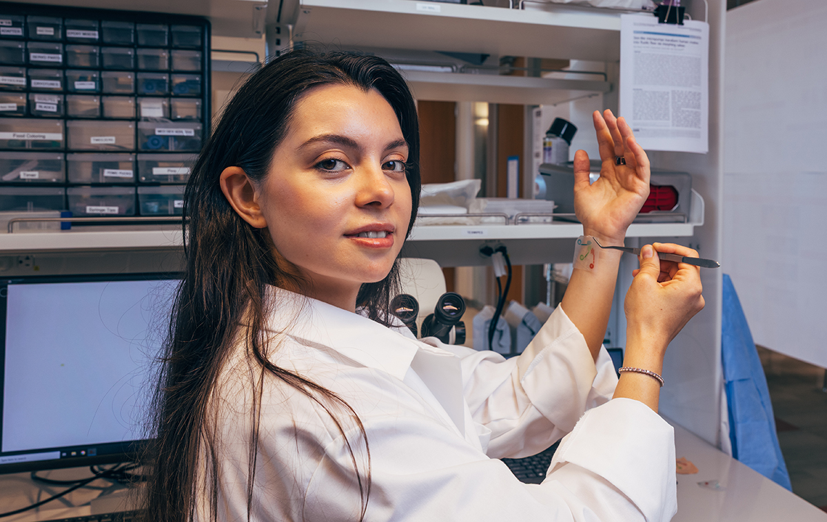 Rana Altay Ph.D. ’26 places the OSMiPump (a small piece of adhesive plastic) to her wrist using tweezers.