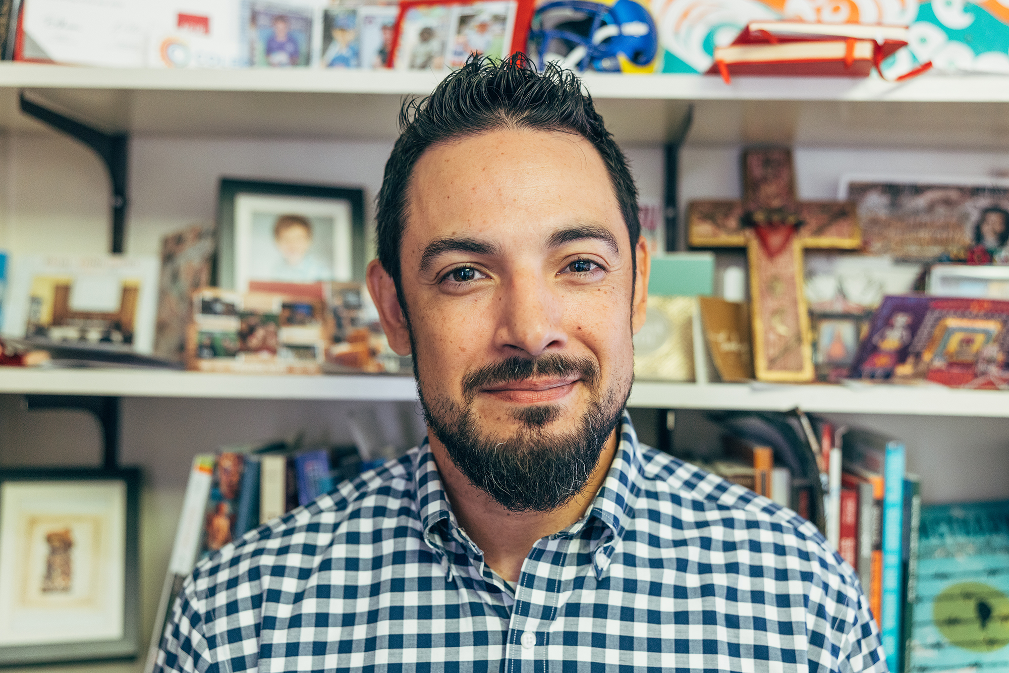 Cruz Medina sits in front of his bookshelf with various knick knacks