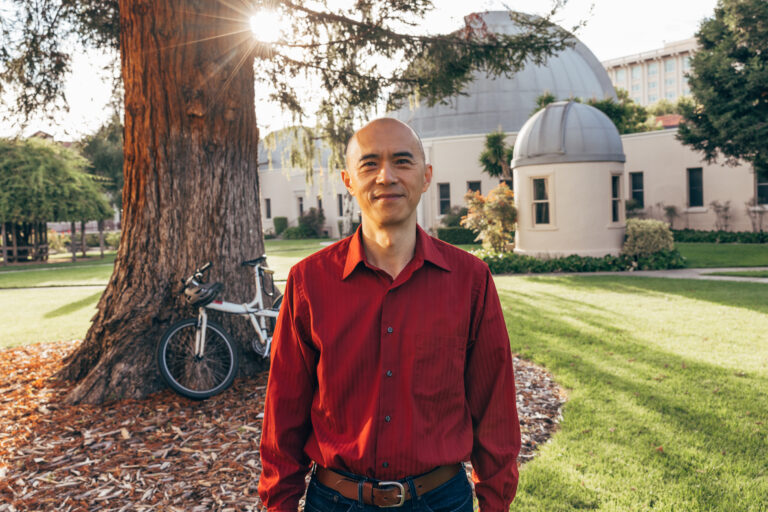 Man smiles while standing in front of tree.