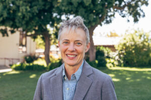 person smiles at camera in gray suit jacket.