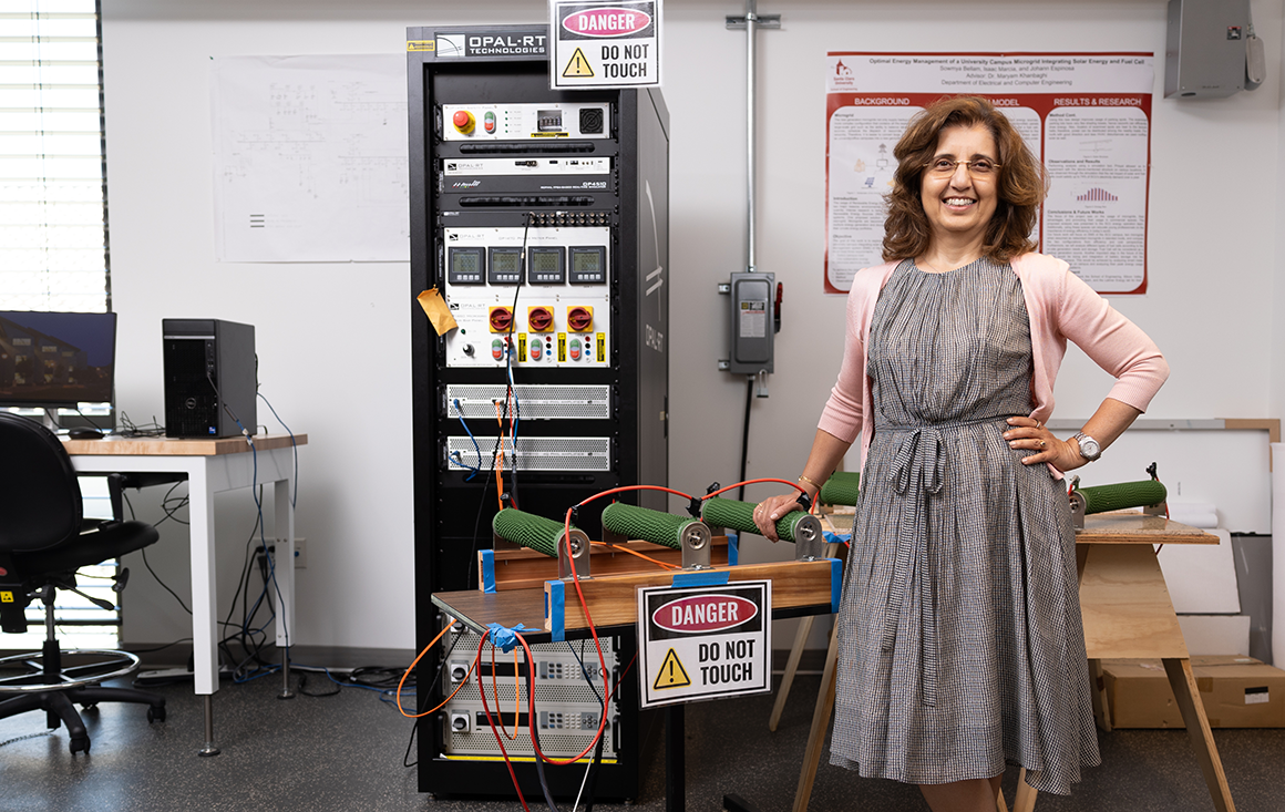 A woman stands next to complicated machinery in a lab.