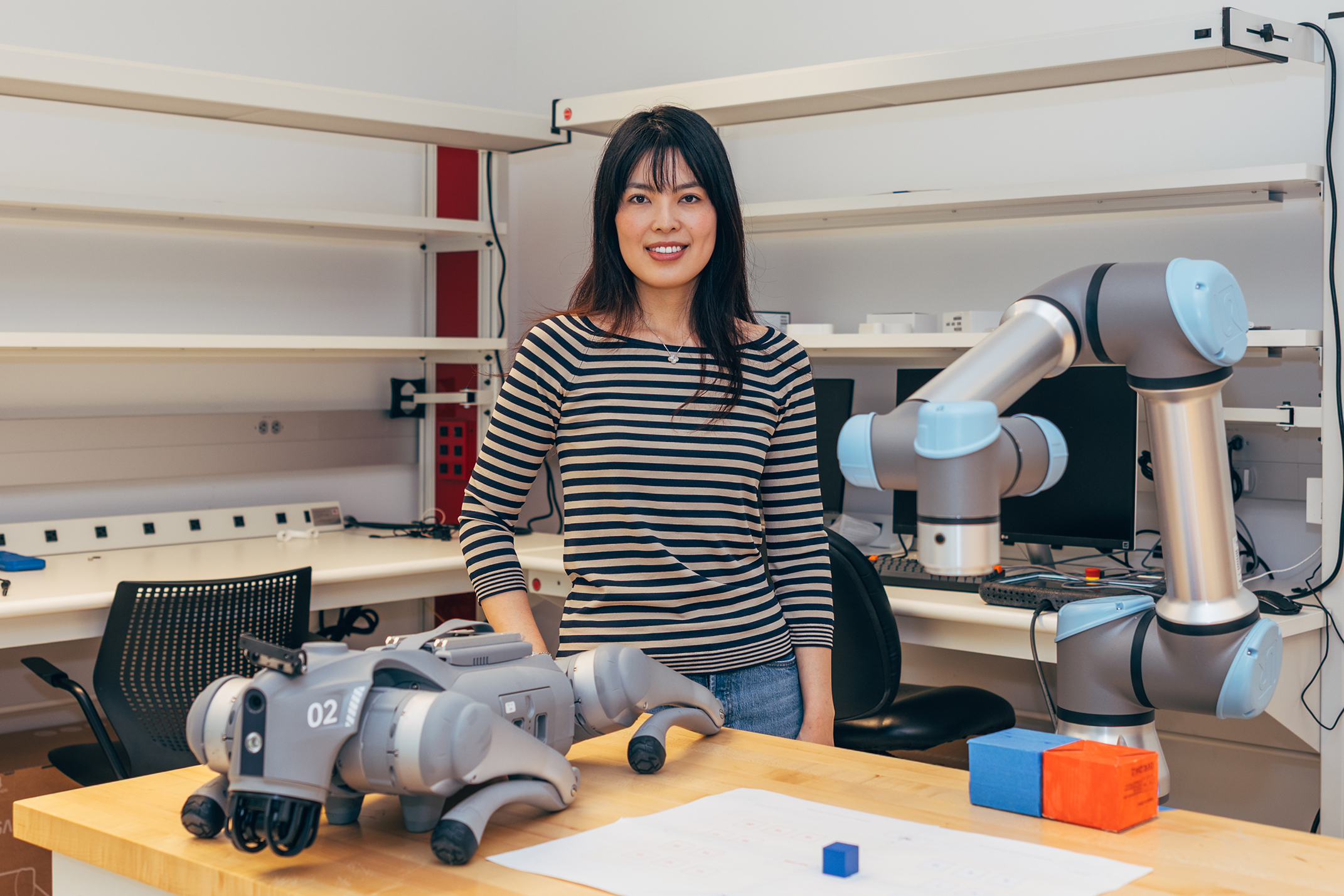 Woman in striped shirt stands over table with robotics sitting on table.