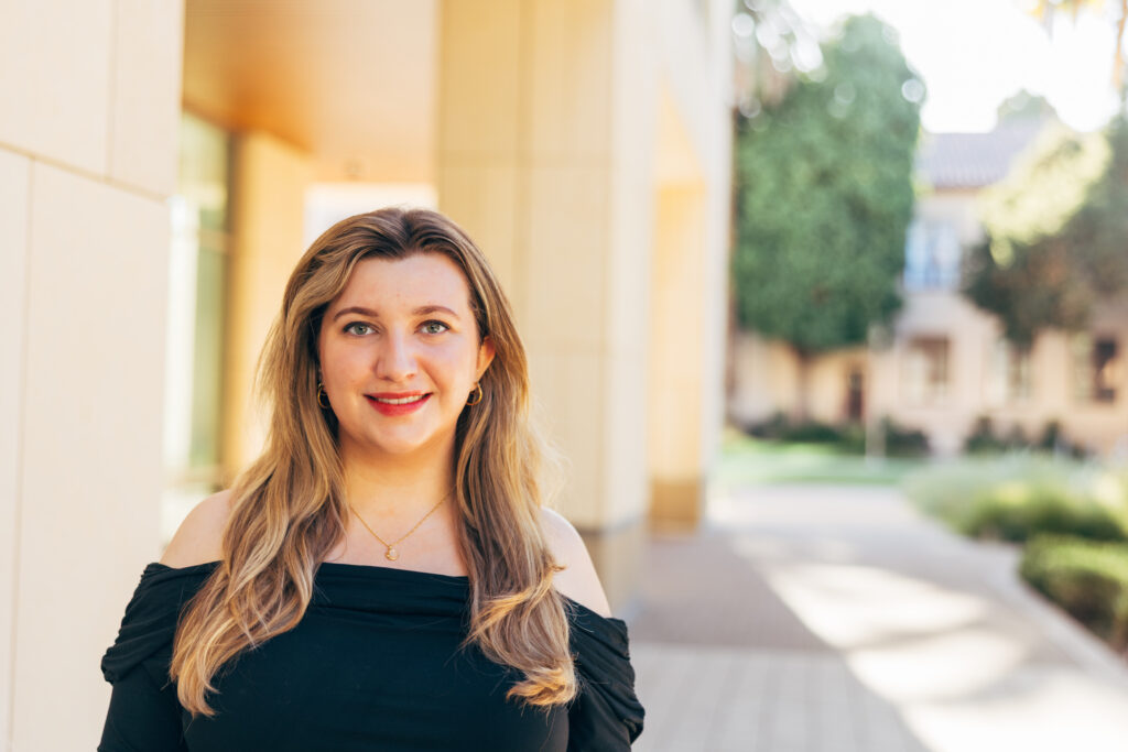 A blonde woman stands next to a large campus building.